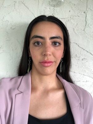 Woman in a light pink blazer looking into camera with a straight face.