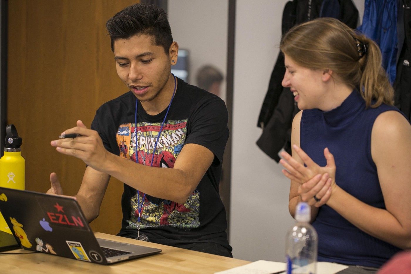 A man and a woman are animatedly talking together while looking onto the same laptop screen.