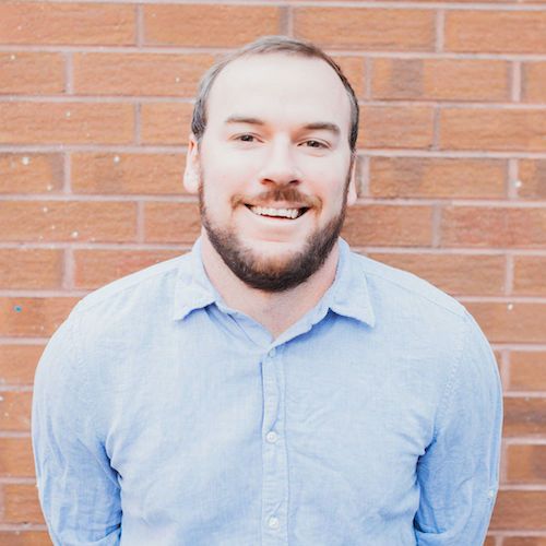 Man standing in front of a brick wall and smiling.